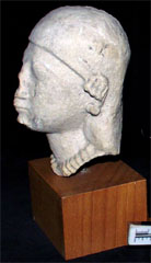 Limestone head of woman wearing cap on head and large earrings and a necklace (AN1938.351)